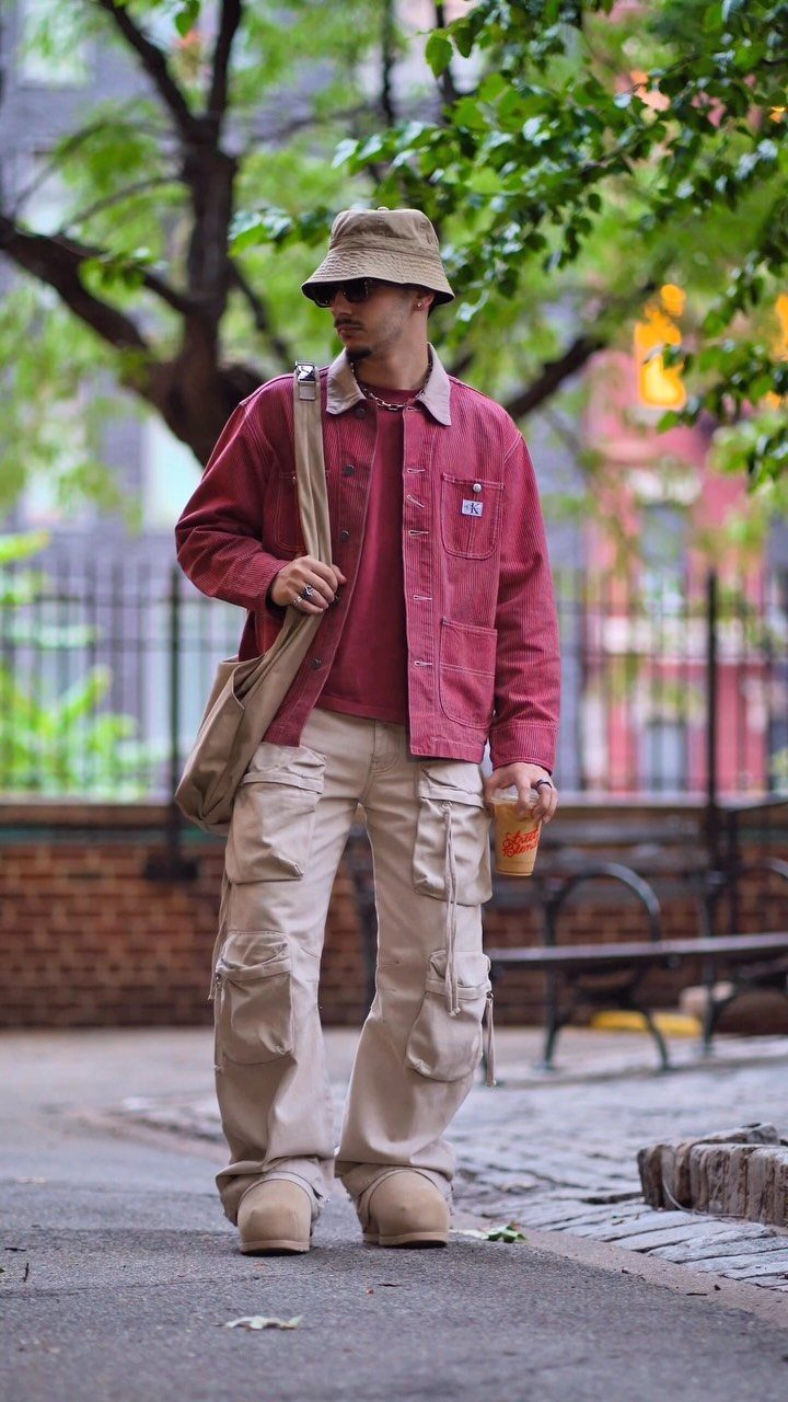 Man wearing a tan bucket hat, red shirt, and beige cargo pants walking outdoors.