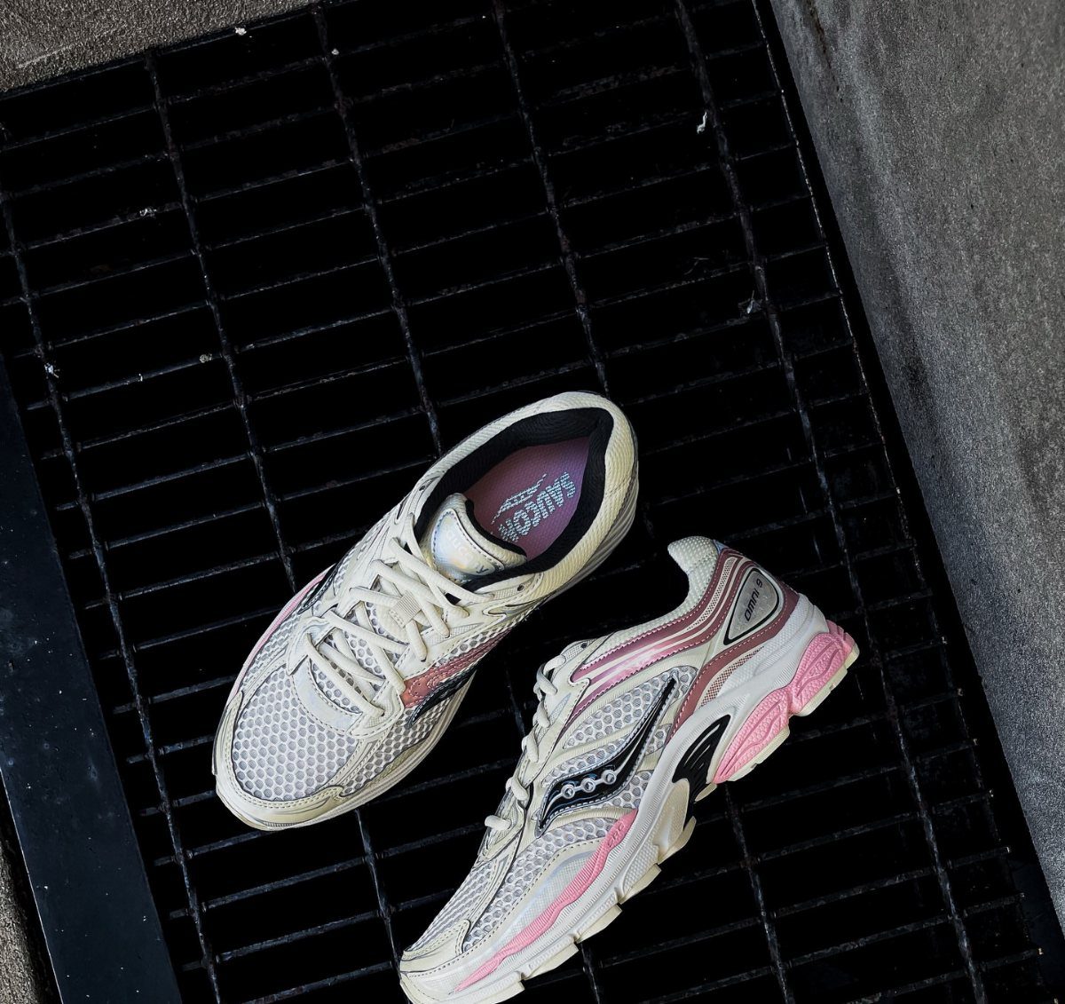White and pink mesh running sneakers resting on a black metal grate.