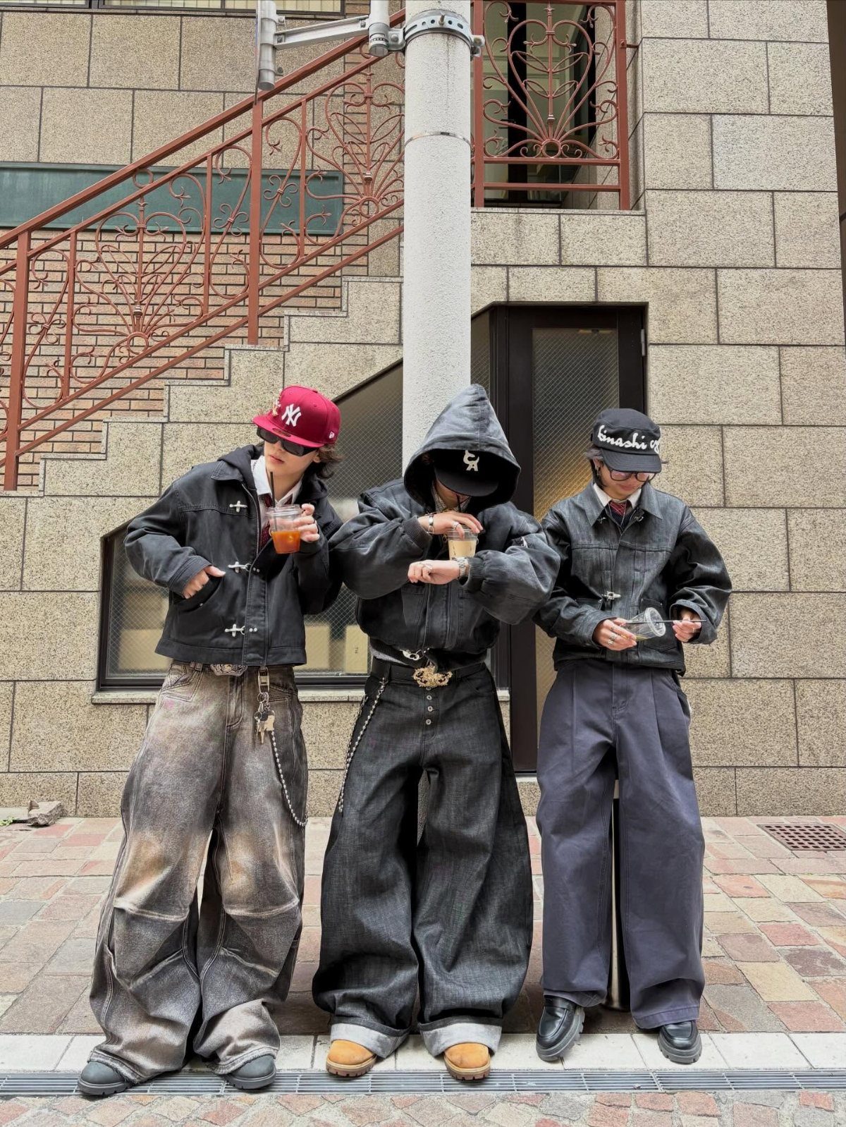 Three people posing in baggy, oversized Japanese streetwear and wide-leg denim trousers outdoors.
