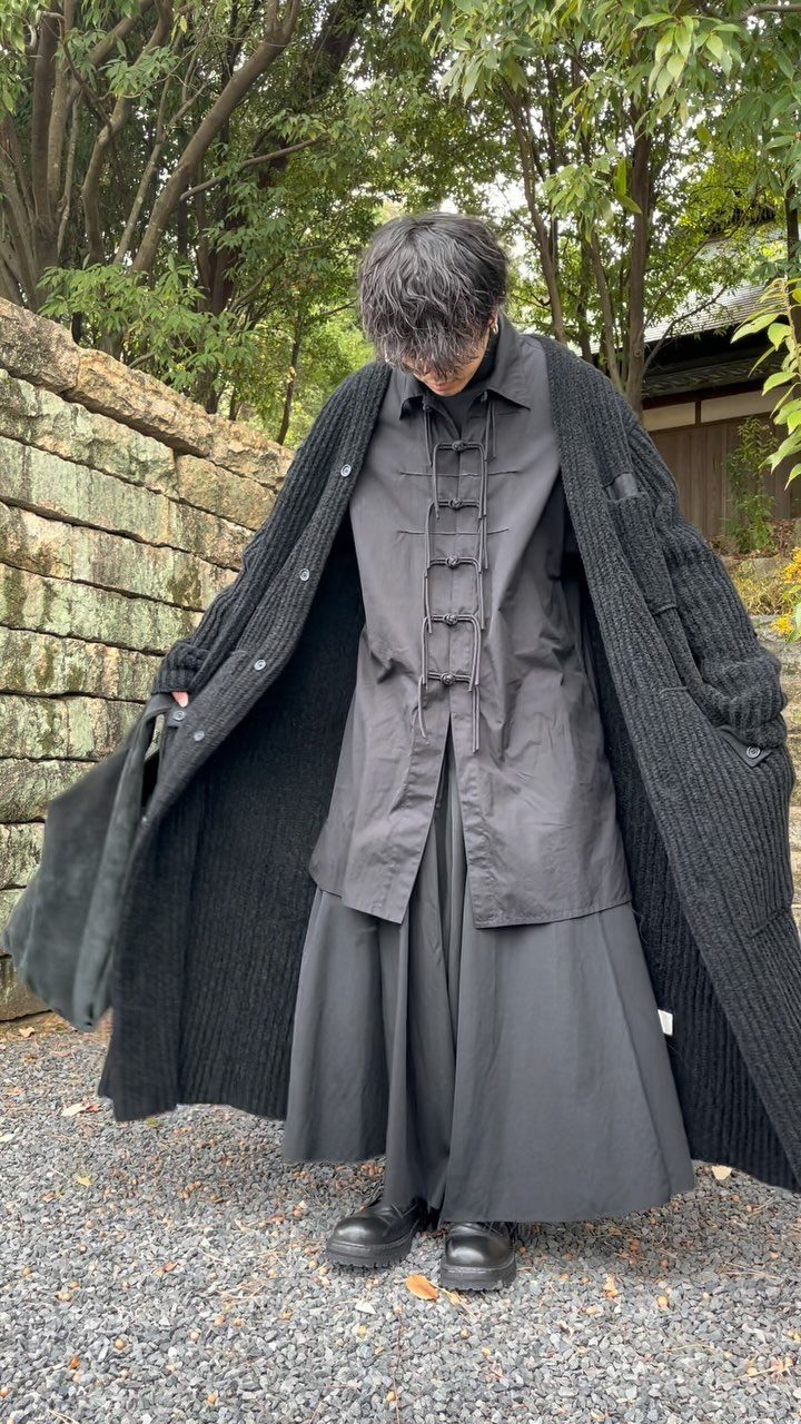 A person wearing an oversized black layered outfit with a long cardigan and wide pleated skirt.