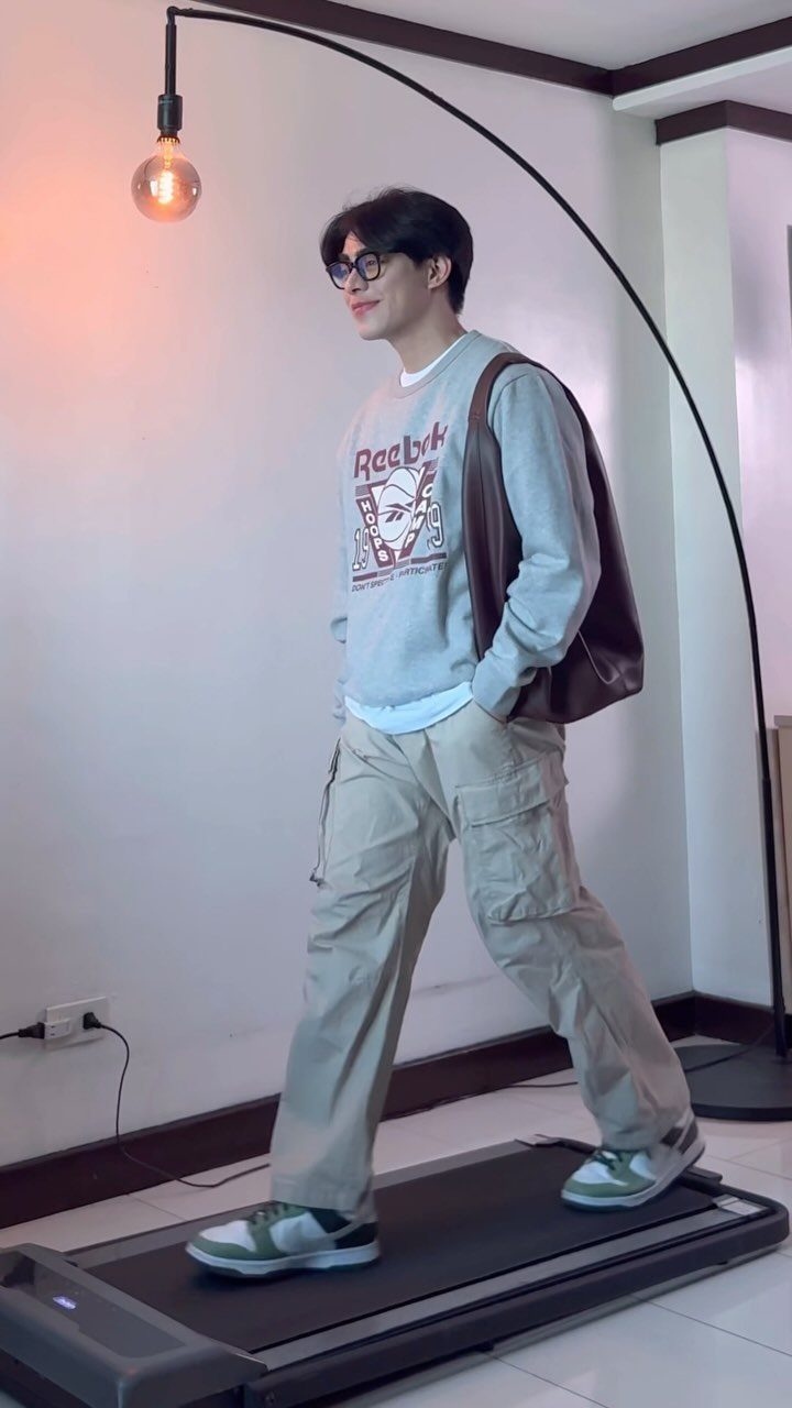 A man in a grey sweatshirt and beige cargo pants walking on a treadmill.
