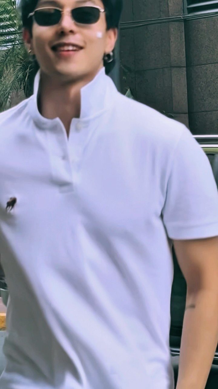 Smiling man wearing dark sunglasses and a white polo shirt with a popped collar.