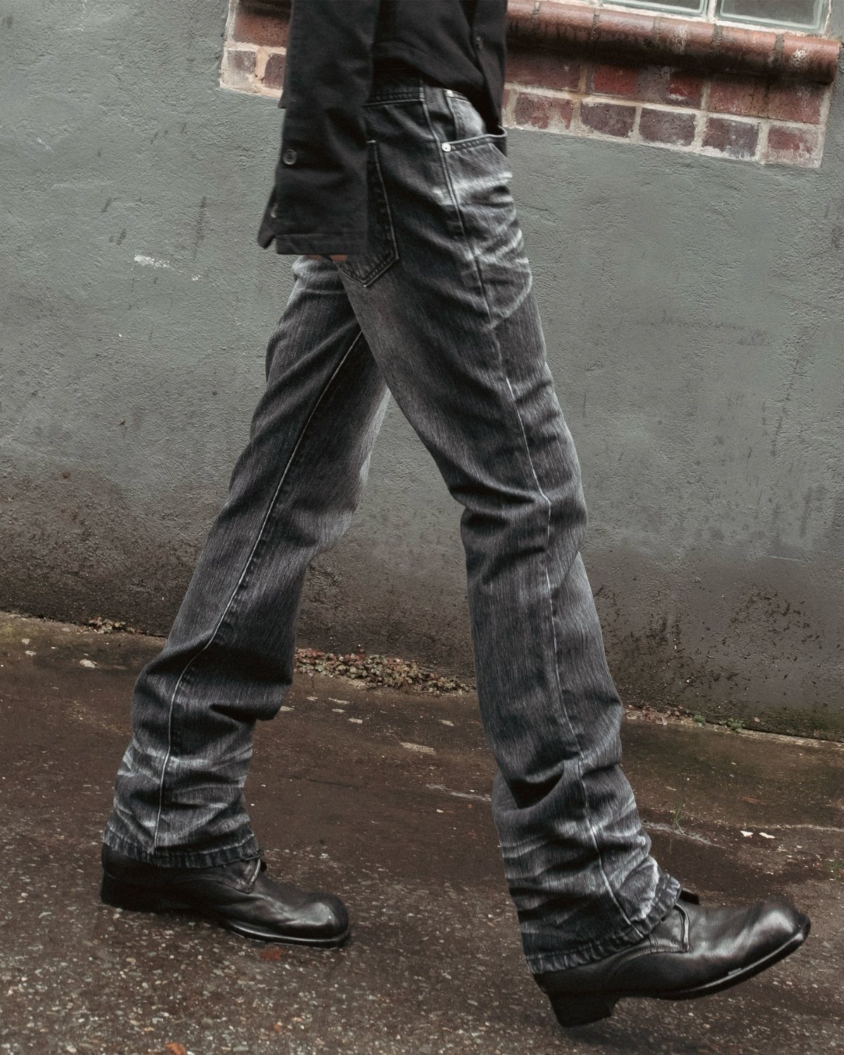 A person walking in dark grey washed denim jeans and black leather shoes.