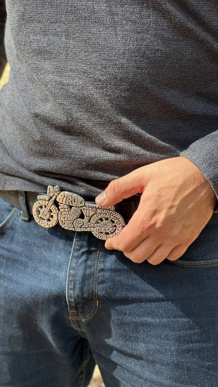 A large, decorative silver motorcycle-shaped belt buckle on blue denim jeans.