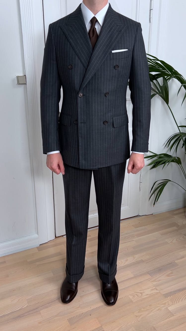 A man standing in a dark grey pinstripe double-breasted suit with a brown tie.