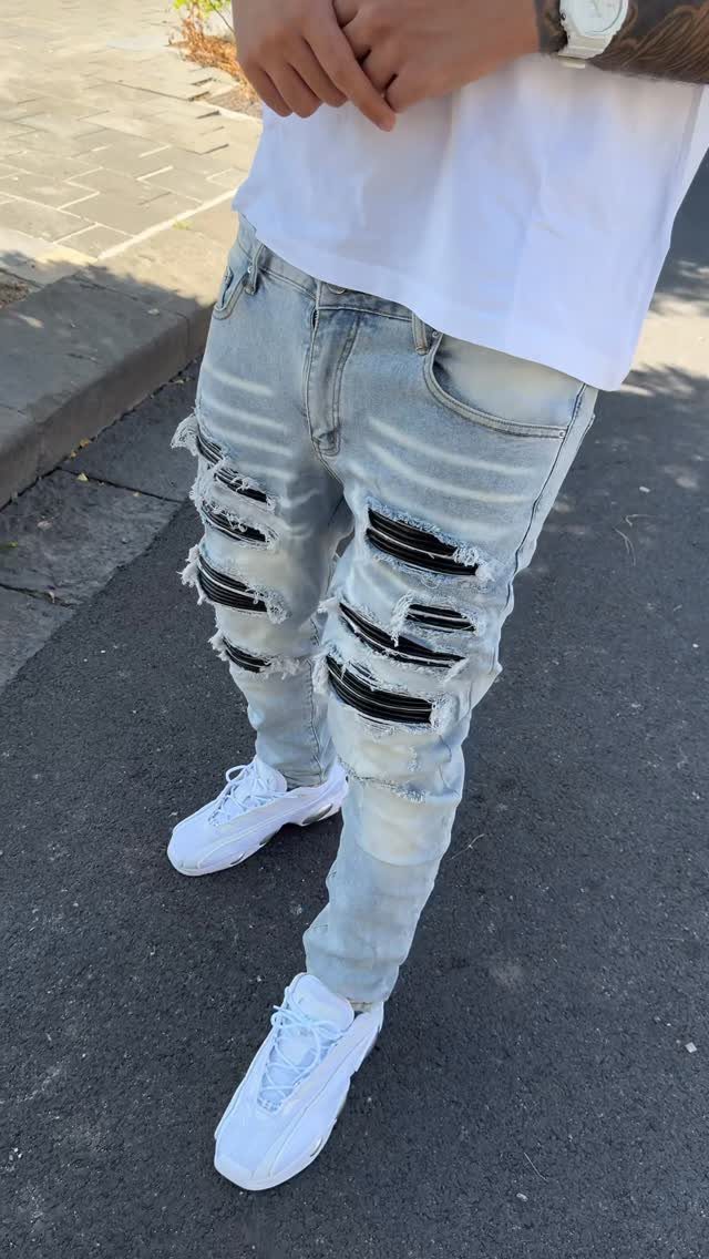 A person wearing light blue distressed skinny jeans with black patches and white sneakers.