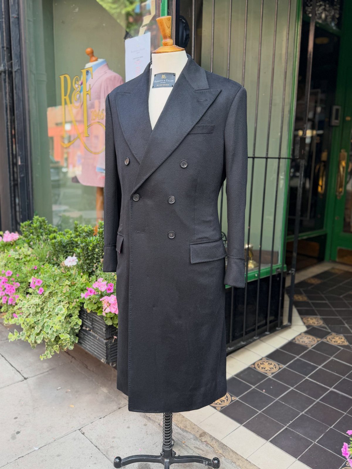 A long charcoal grey double-breasted topcoat with peak lapels on a mannequin.
