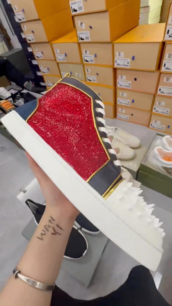 A hand holds a red glittery high-top sneaker with white spikes and black trim.