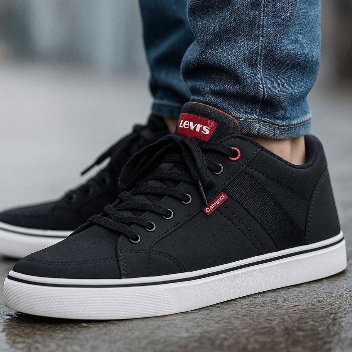 Black canvas casual sneakers with white soles worn with blue denim jeans on a paved surface.