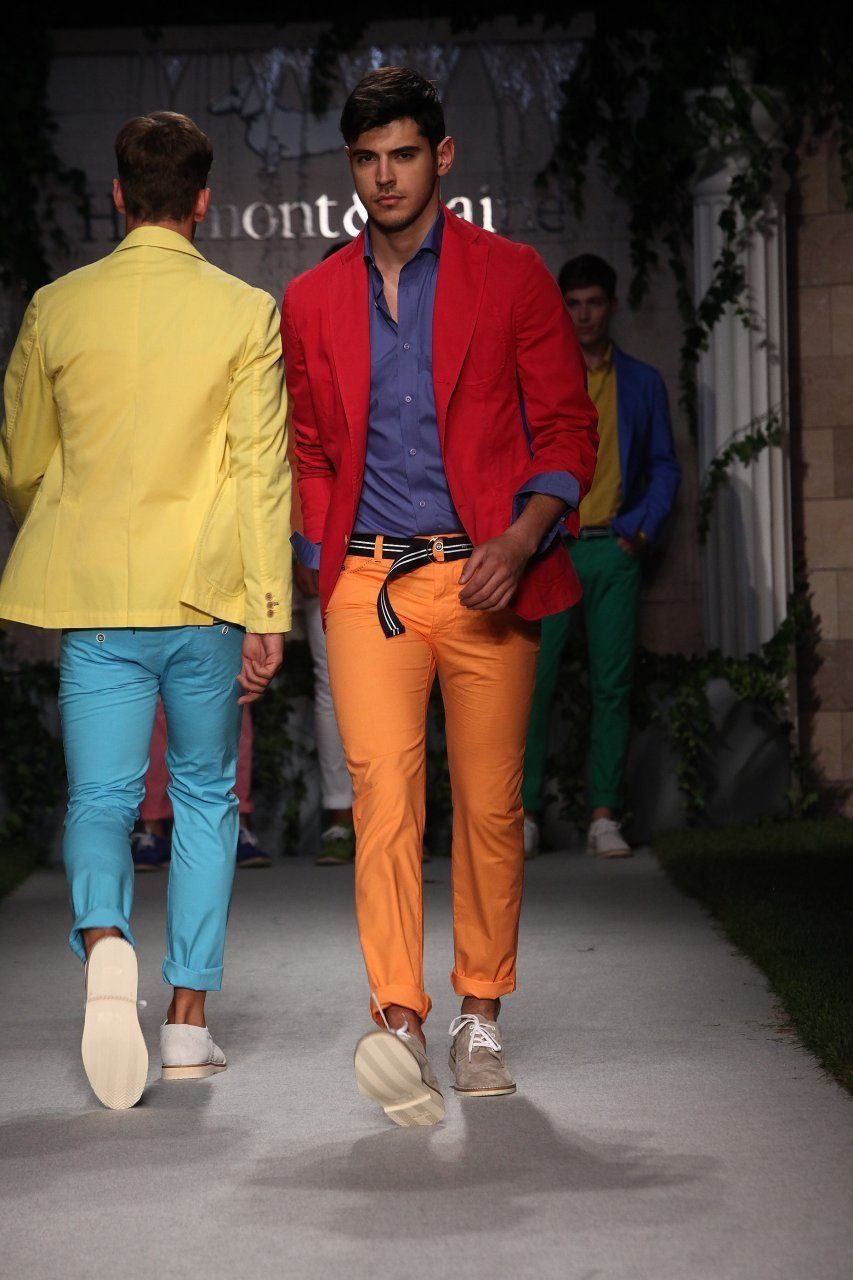 Male models walking a runway in bright red, blue, orange, and yellow fashion outfits.