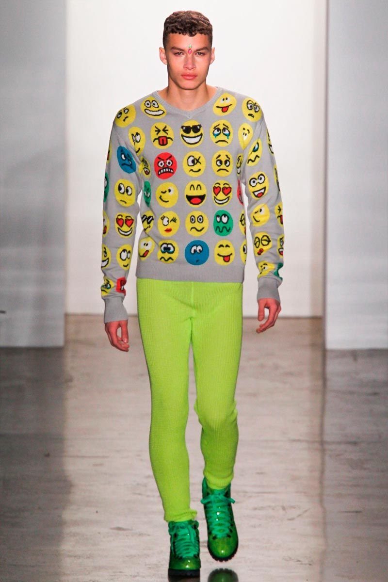 A male model walking a runway in a grey emoji sweater and lime green trousers.