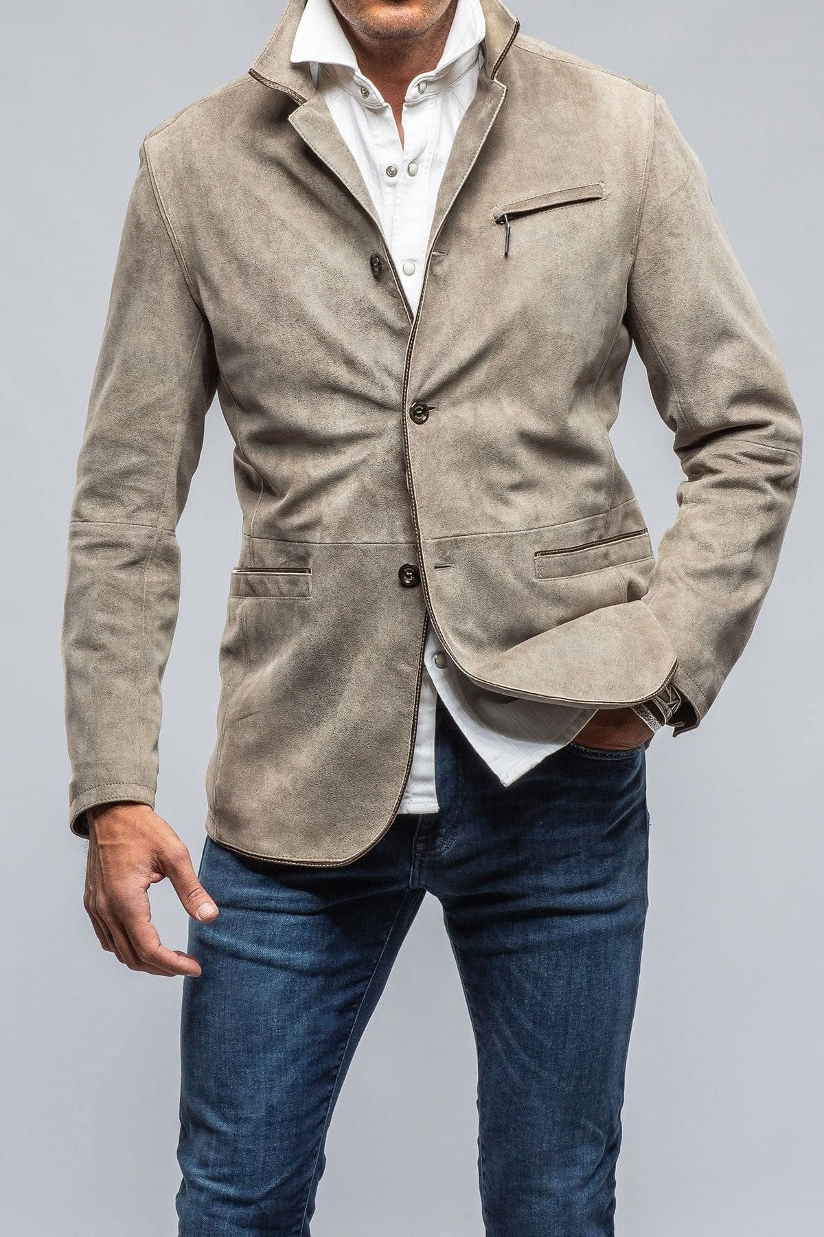 A man wearing a fitted light brown suede blazer, white shirt, and blue jeans.
