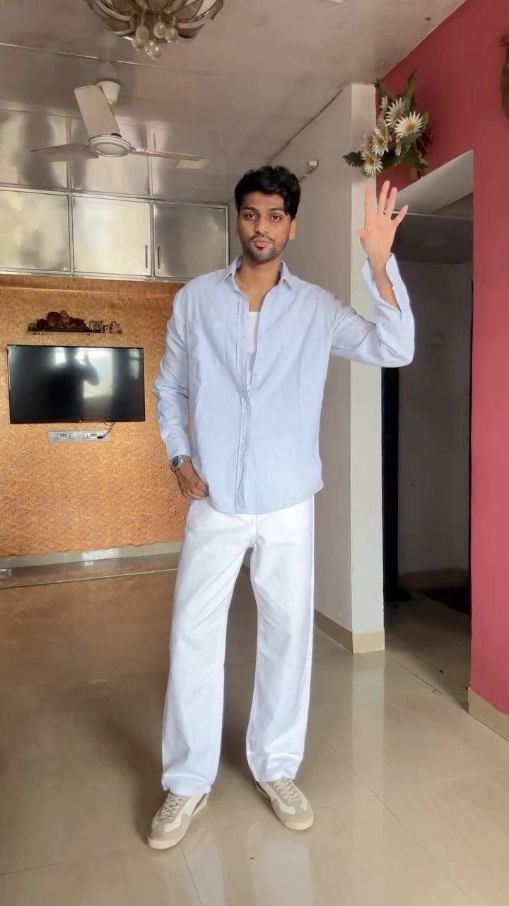 A man posing in a light blue shirt and wide-leg white trousers with beige sneakers.
