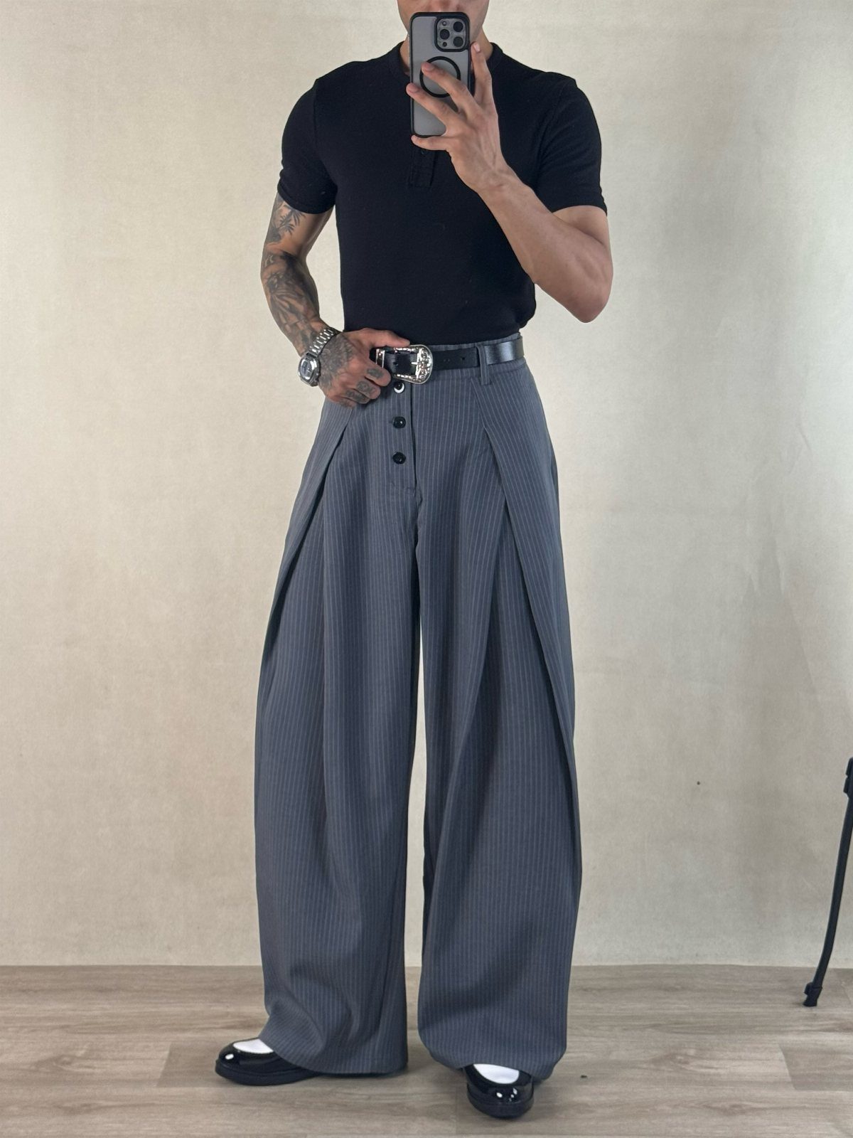 A person wearing wide grey pinstriped baggy trousers, a black shirt, and black shoes.