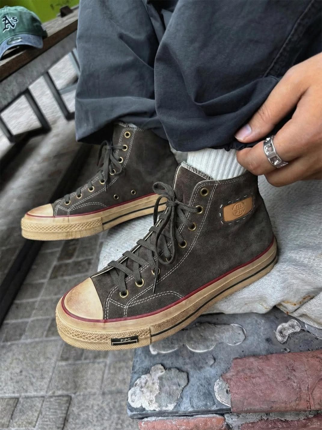 Person wearing distressed brown high-top canvas sneakers with white socks and dark trousers.