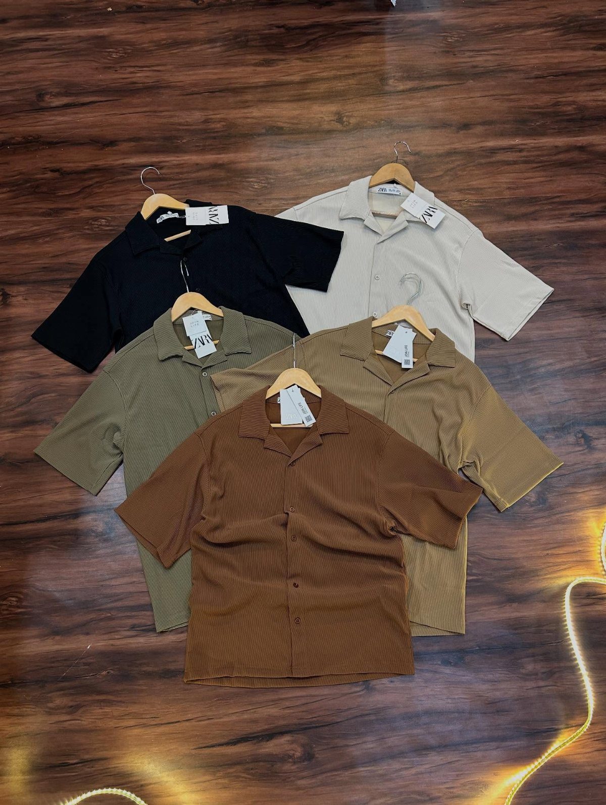 Five short-sleeved shirts with Cuban collars arranged on a dark wooden floor.