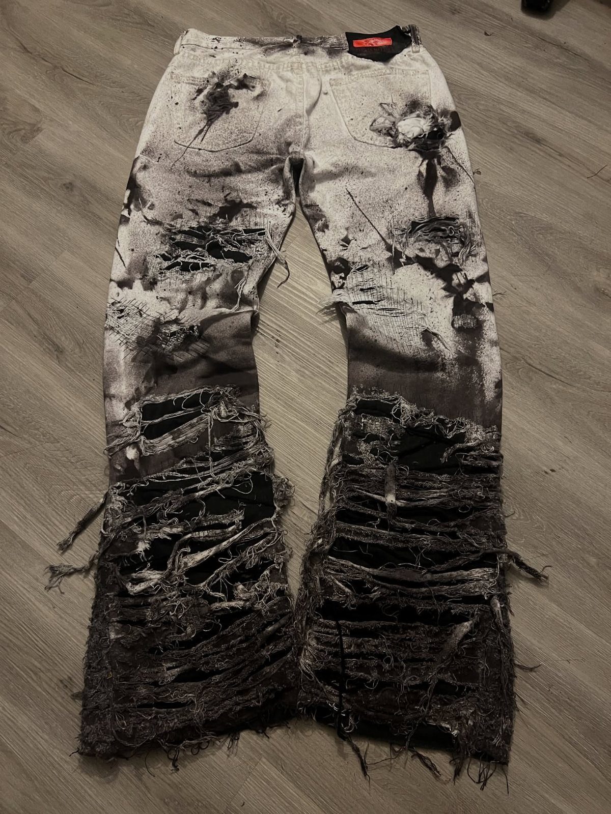 Heavily distressed black and white patterned denim jeans lying on a light wooden floor.