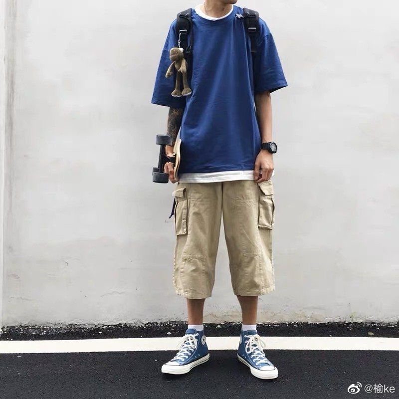 A person wearing a blue t-shirt, tan cargo shorts, and blue high-top sneakers standing outdoors.
