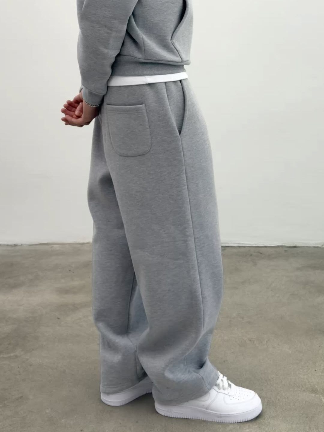 A person wearing a grey sweatshirt, white undershirt, and baggy grey sweatpants with white sneakers.