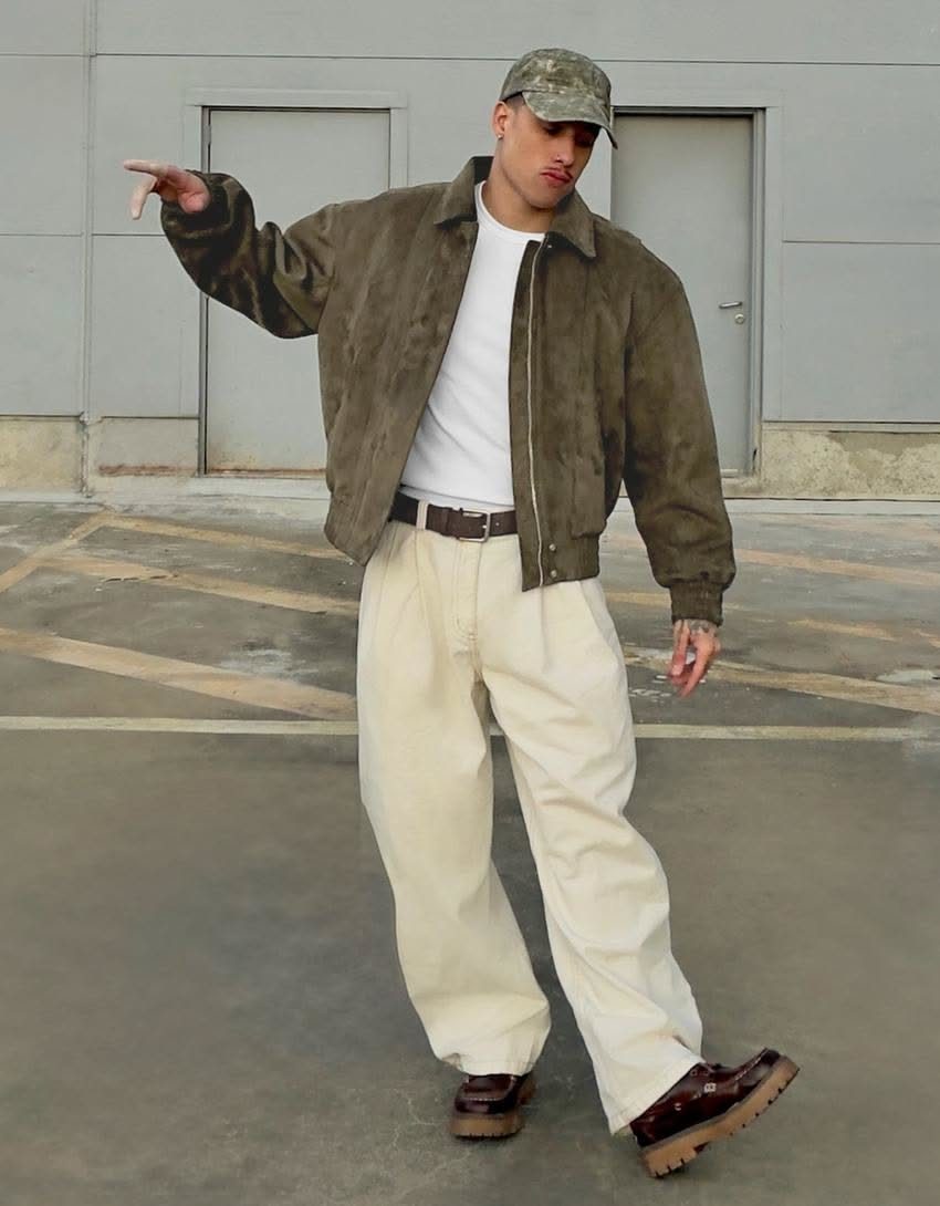 Man wearing an olive green suede jacket, white t-shirt, and cream baggy trousers.