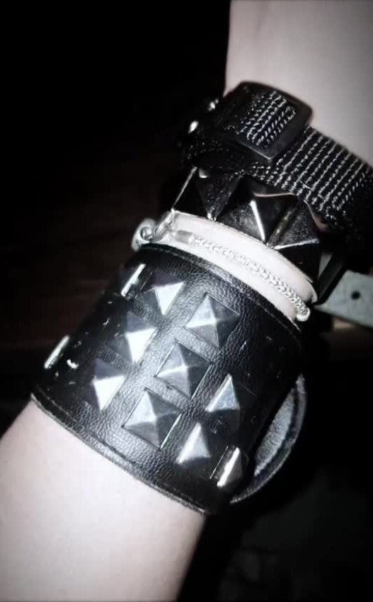 A wrist adorned with a wide black leather cuff featuring large silver pyramid studs.