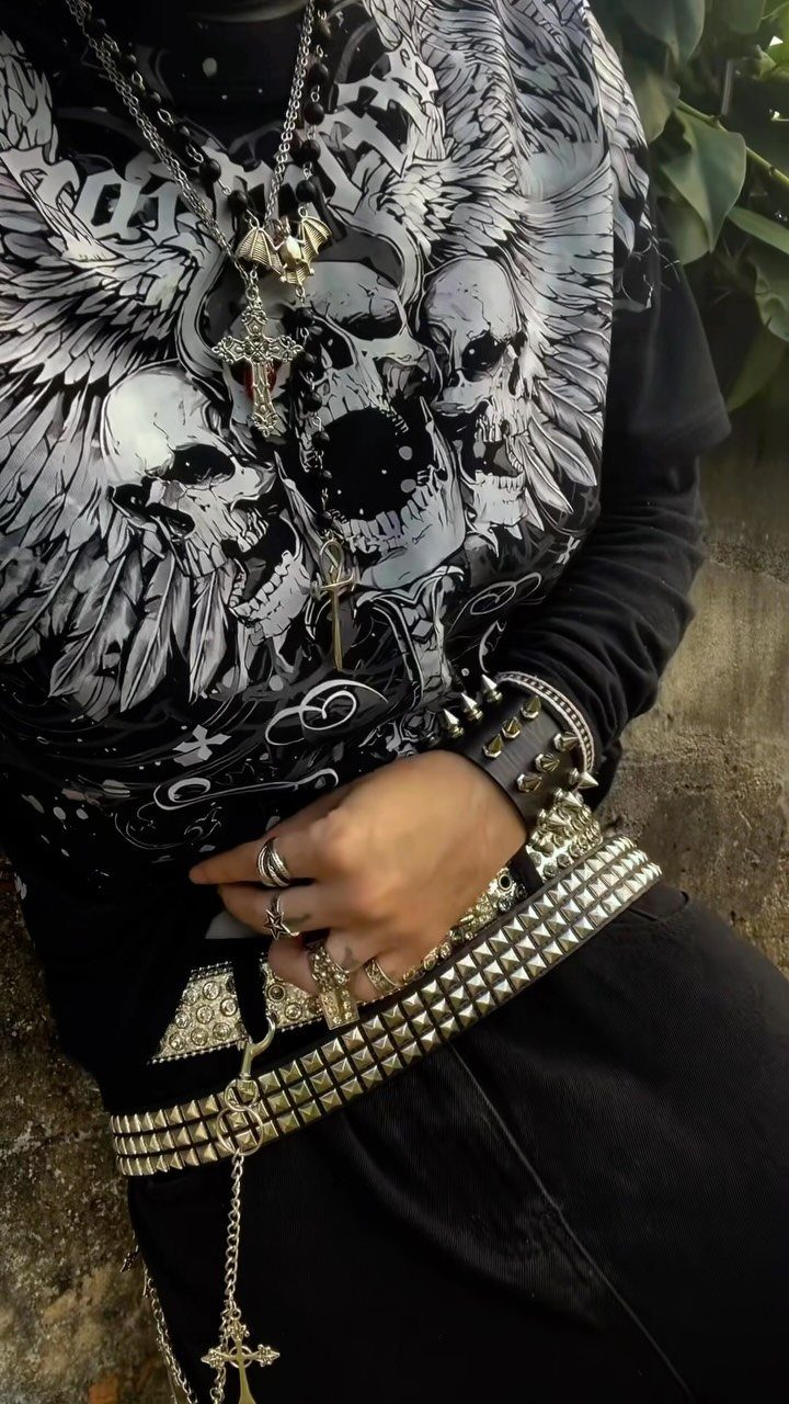 Person wearing a black skull graphic t-shirt, silver necklaces, and a wide silver studded belt.