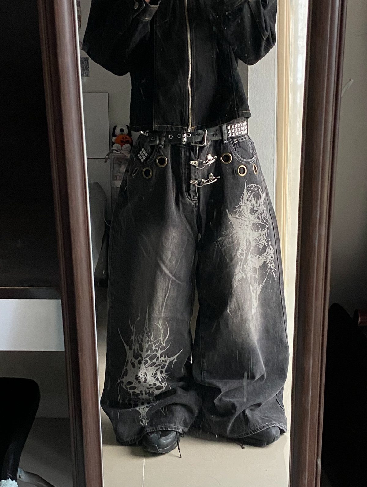 Person wearing baggy black graphic denim jeans with a studded belt and black top.