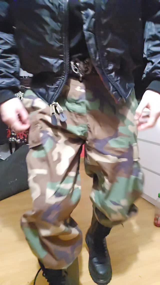 A person wearing a black bomber jacket, camouflage cargo pants, and black boots.