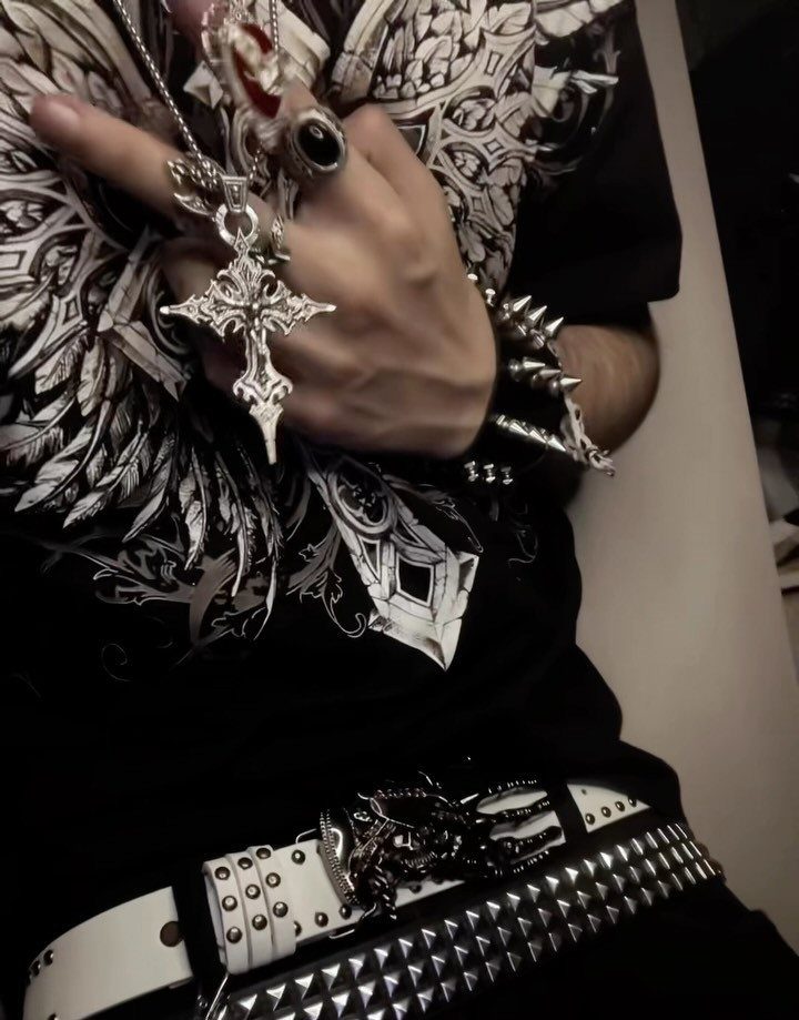 A person wearing black graphic clothing, silver jewelry, and multiple white studded belts.