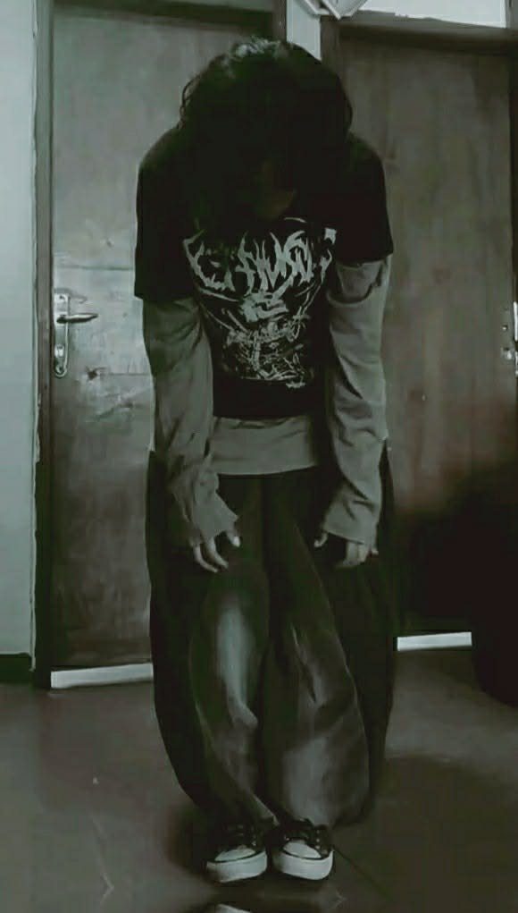 Person wearing a black graphic t-shirt layered over long sleeves and baggy dark pants.