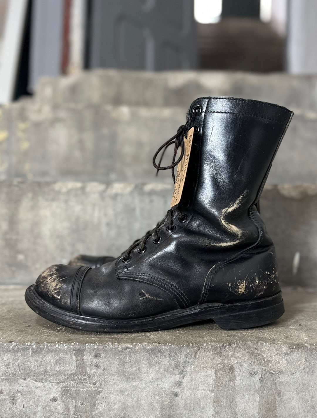 Worn black leather combat boots with scuffs sitting on grey concrete steps.