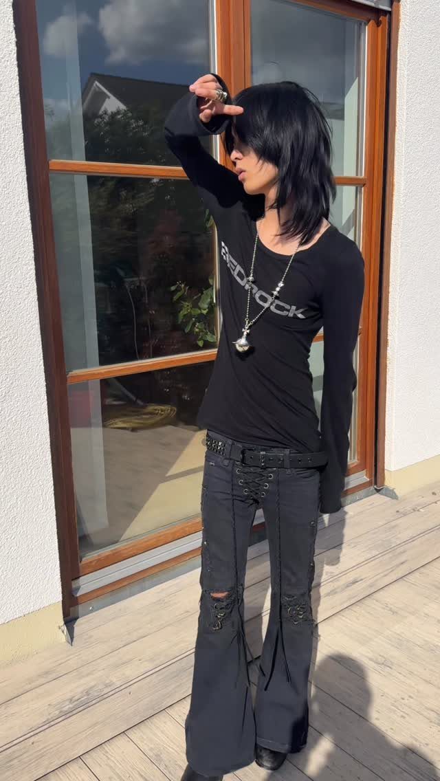 A person in black grunge clothing posing in front of a glass door.