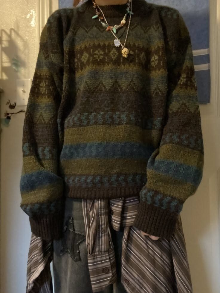 Person wearing an oversized patterned knit sweater with layered necklaces and a striped shirt tied around their waist.