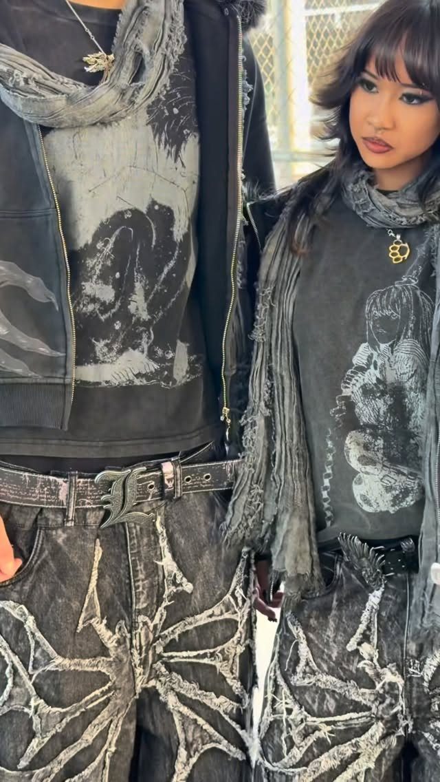Two people wearing distressed black and grey graphic clothing with spiderweb patterns.