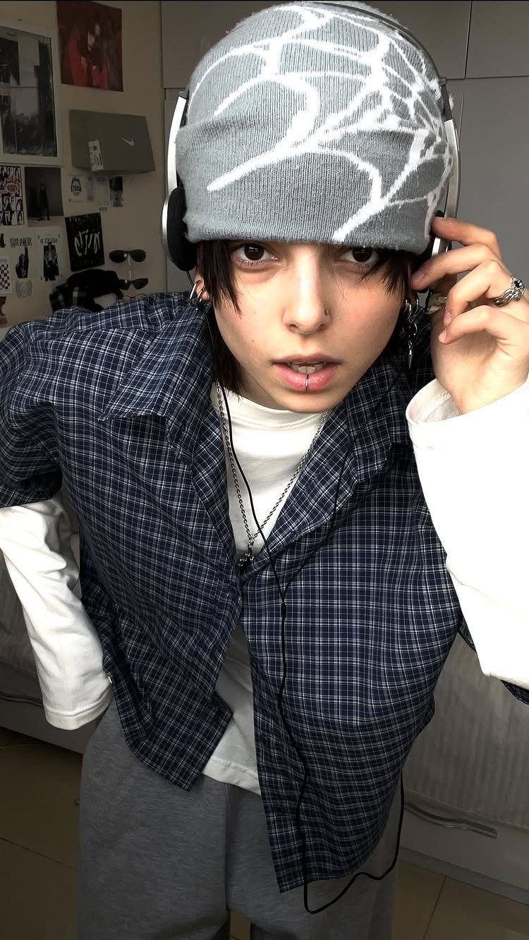 Person wearing a grey beanie, white headphones, and a blue plaid shirt over a white top.