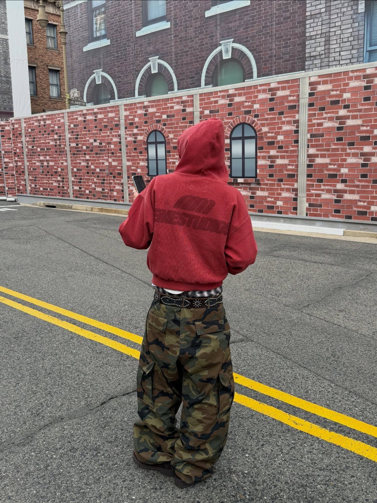 Person in a red ribbed hoodie and camouflage cargo pants standing on a street.