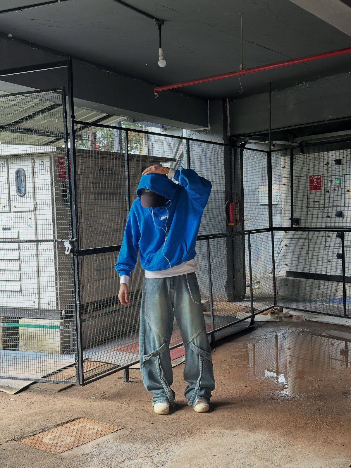 Man wearing a bright blue hoodie and baggy denim jeans standing in an industrial area.