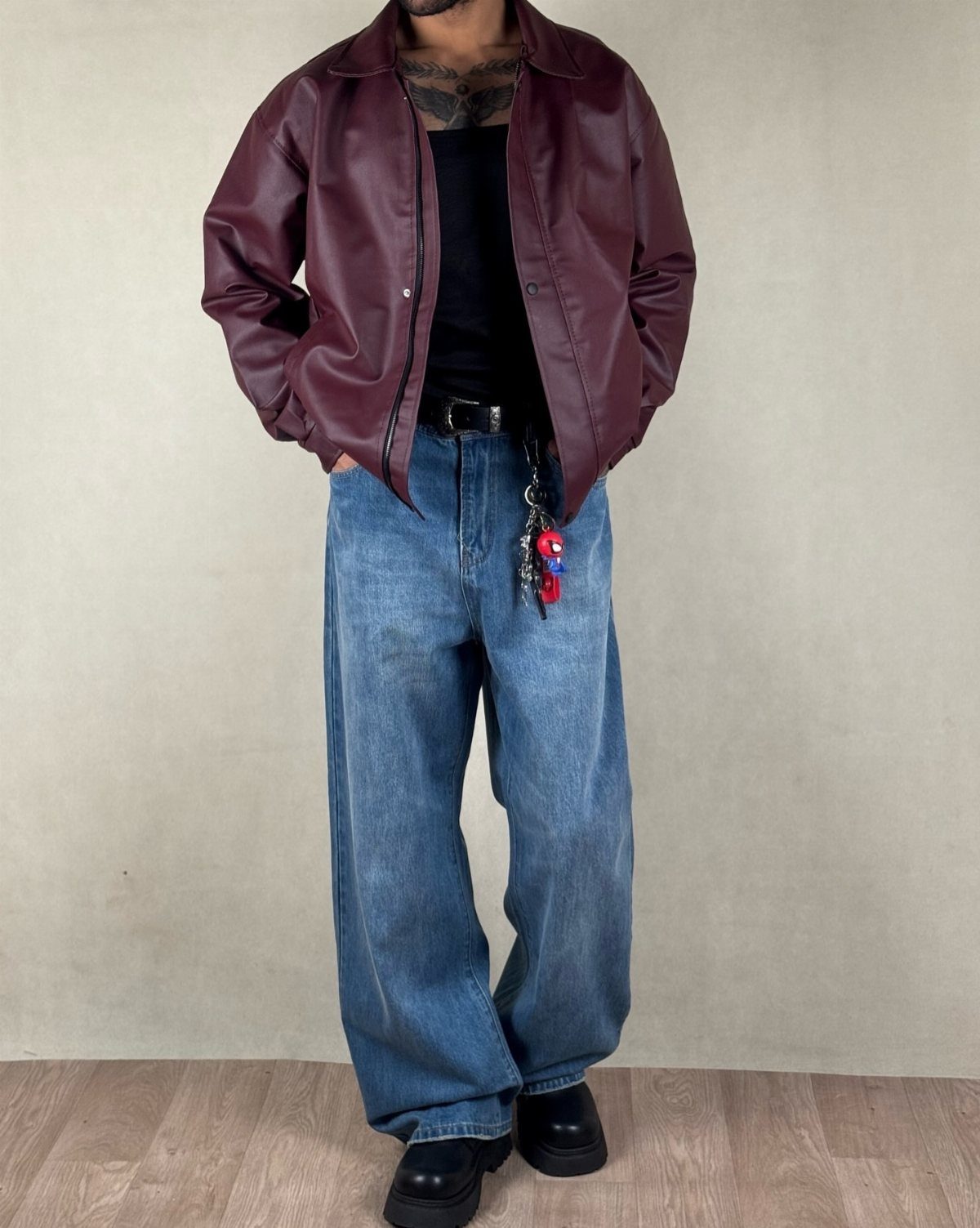 Man wearing a maroon leather jacket, black t-shirt, and baggy blue jeans with black shoes.