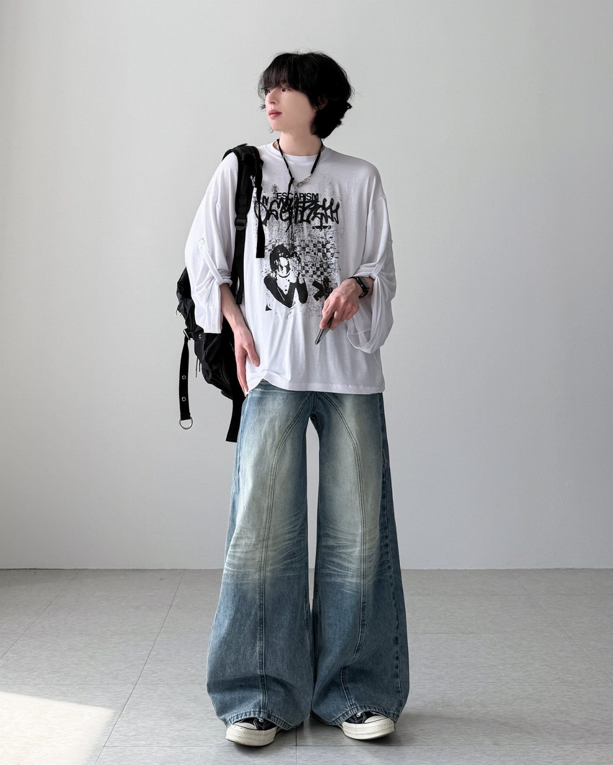 A young man posing in an oversized white shirt and very wide-leg baggy blue jeans.