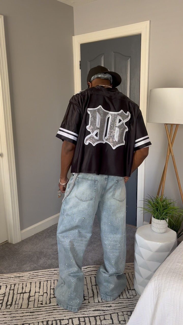 Person wearing a black jersey with white lettering and light blue baggy denim jeans.