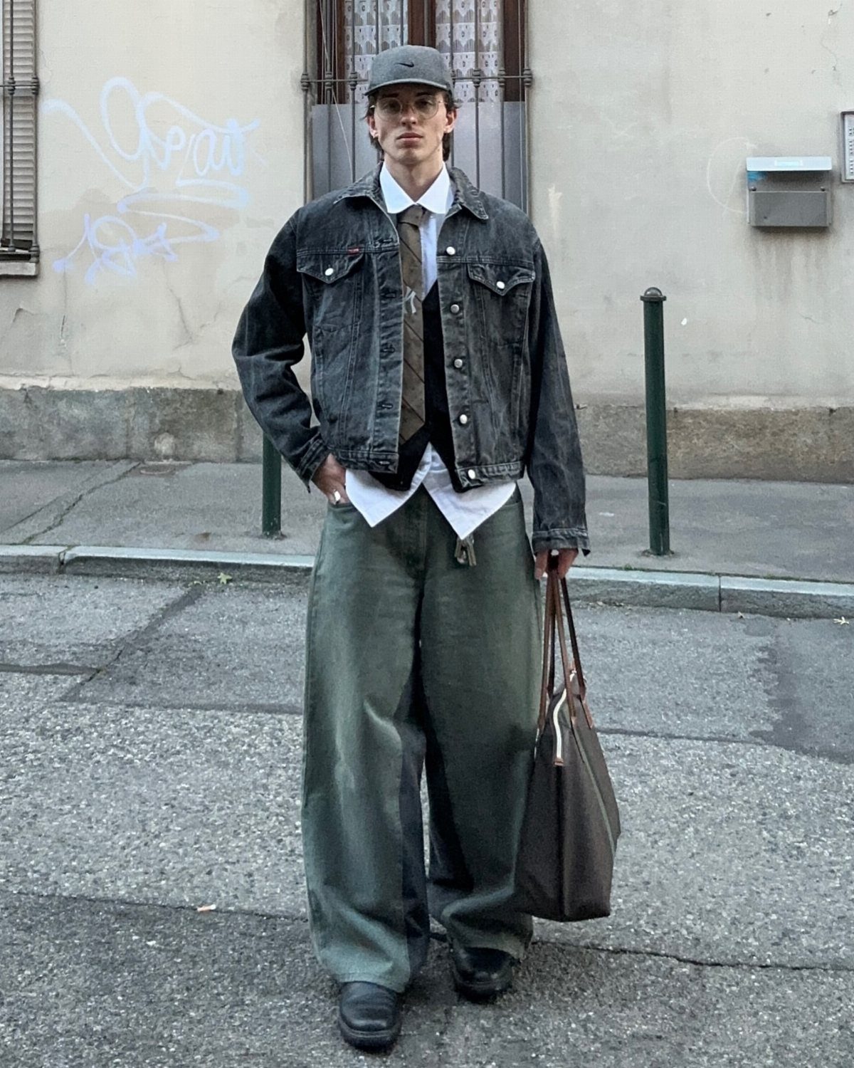 Man wearing an oversized dark denim jacket, white shirt, tie, and extremely wide green baggy trousers.