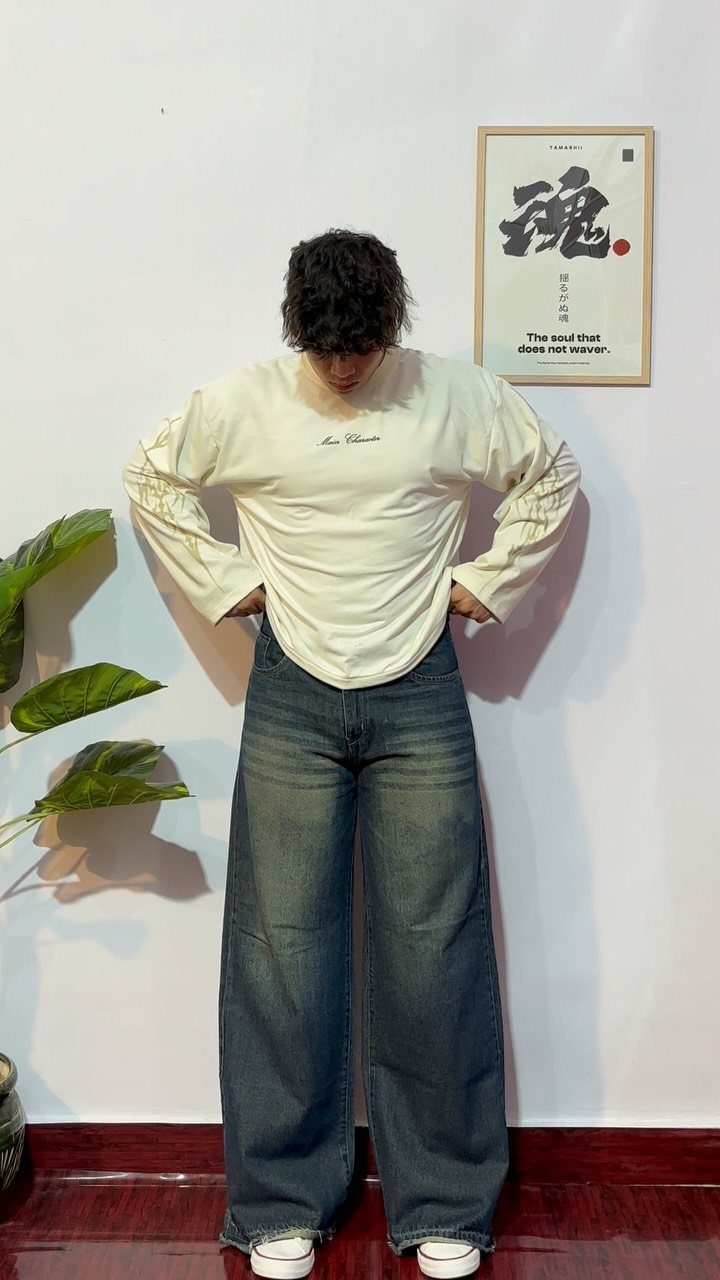 A person wearing an oversized cream long-sleeve shirt and wide-leg baggy blue denim jeans.
