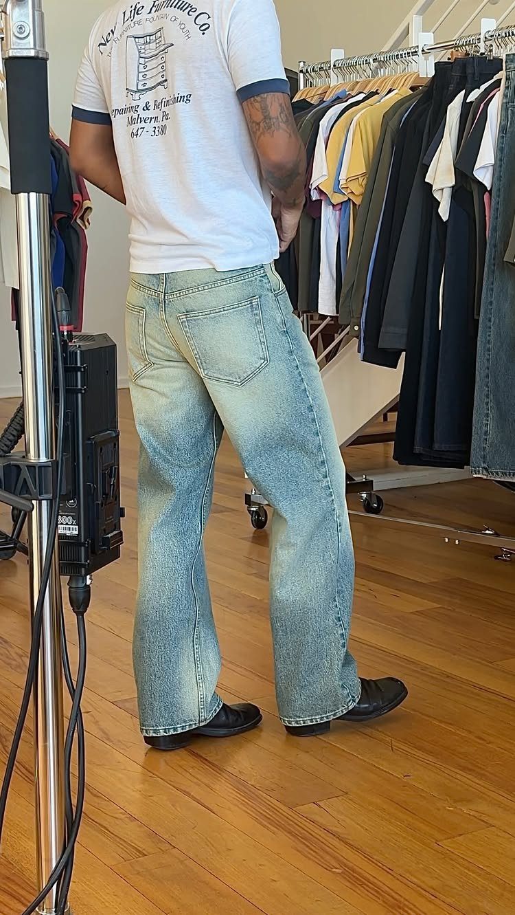 Man wearing light blue baggy denim jeans and a white t-shirt in a clothing store.