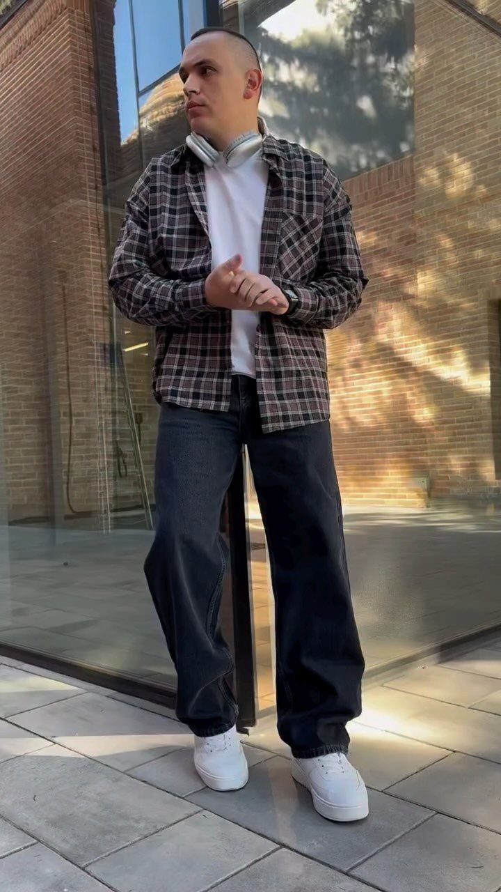 Man wearing a plaid shirt over a white t-shirt and baggy dark jeans.