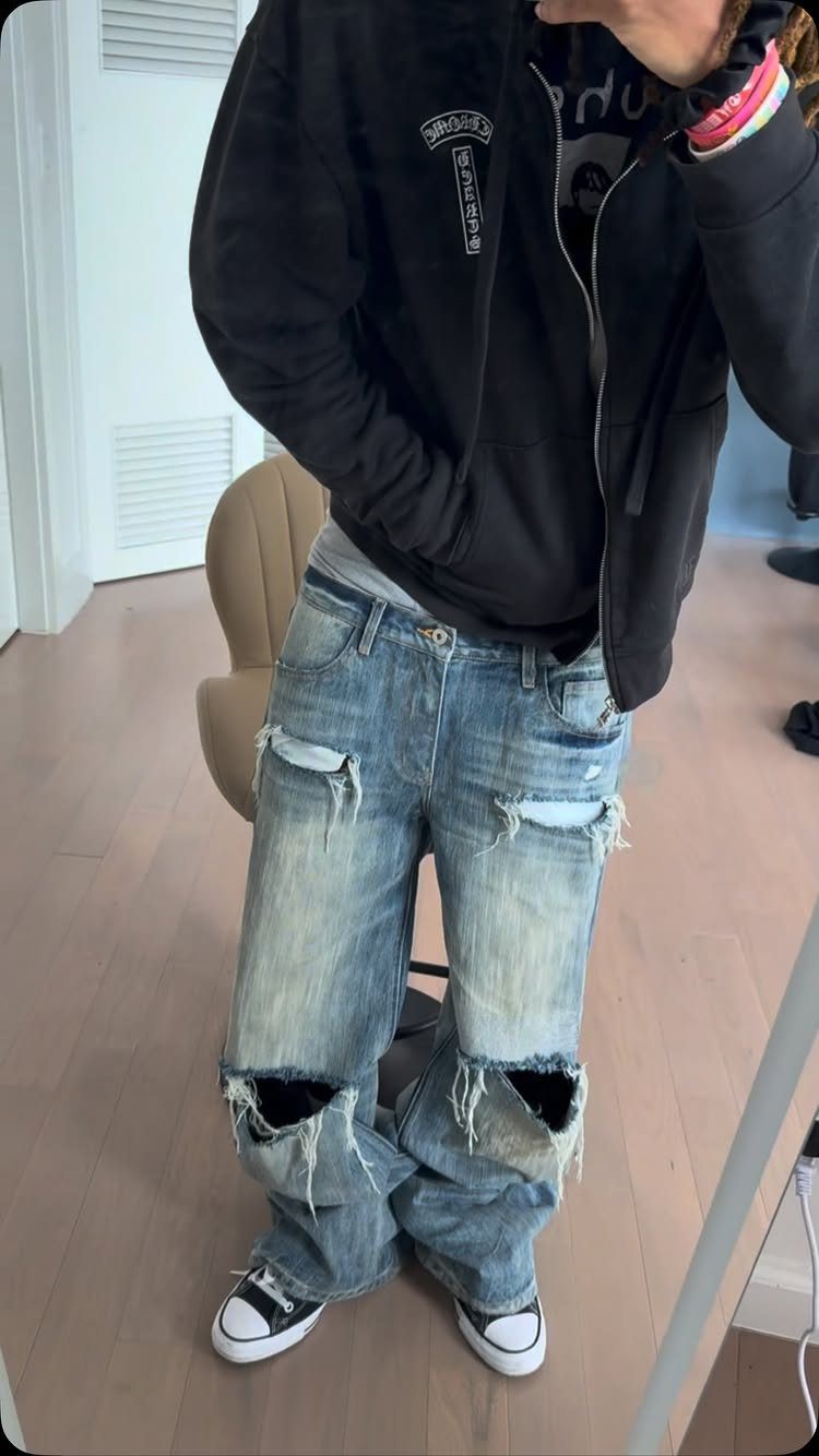 Person wearing baggy light blue distressed jeans with large knee rips and a black hoodie.