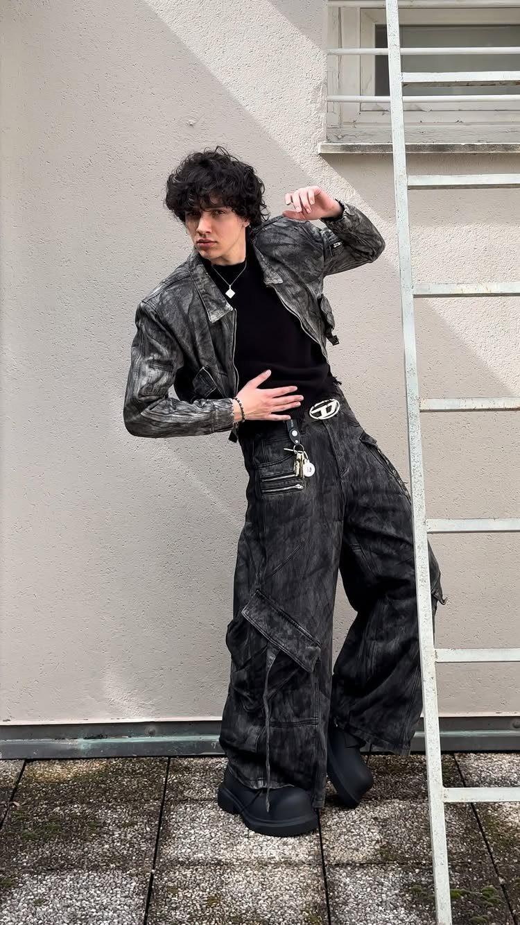 A young man posing in a dark denim jacket and oversized black cargo pants.