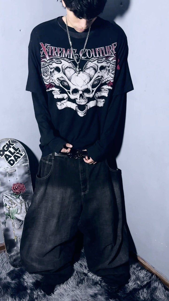 A person wearing a black graphic t-shirt with a skull design and baggy dark pants.