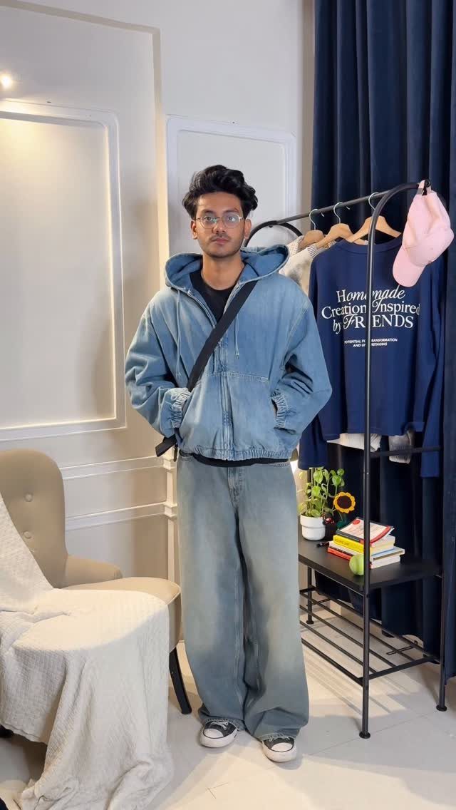 A young man posing in an oversized denim jacket and baggy light blue jeans.