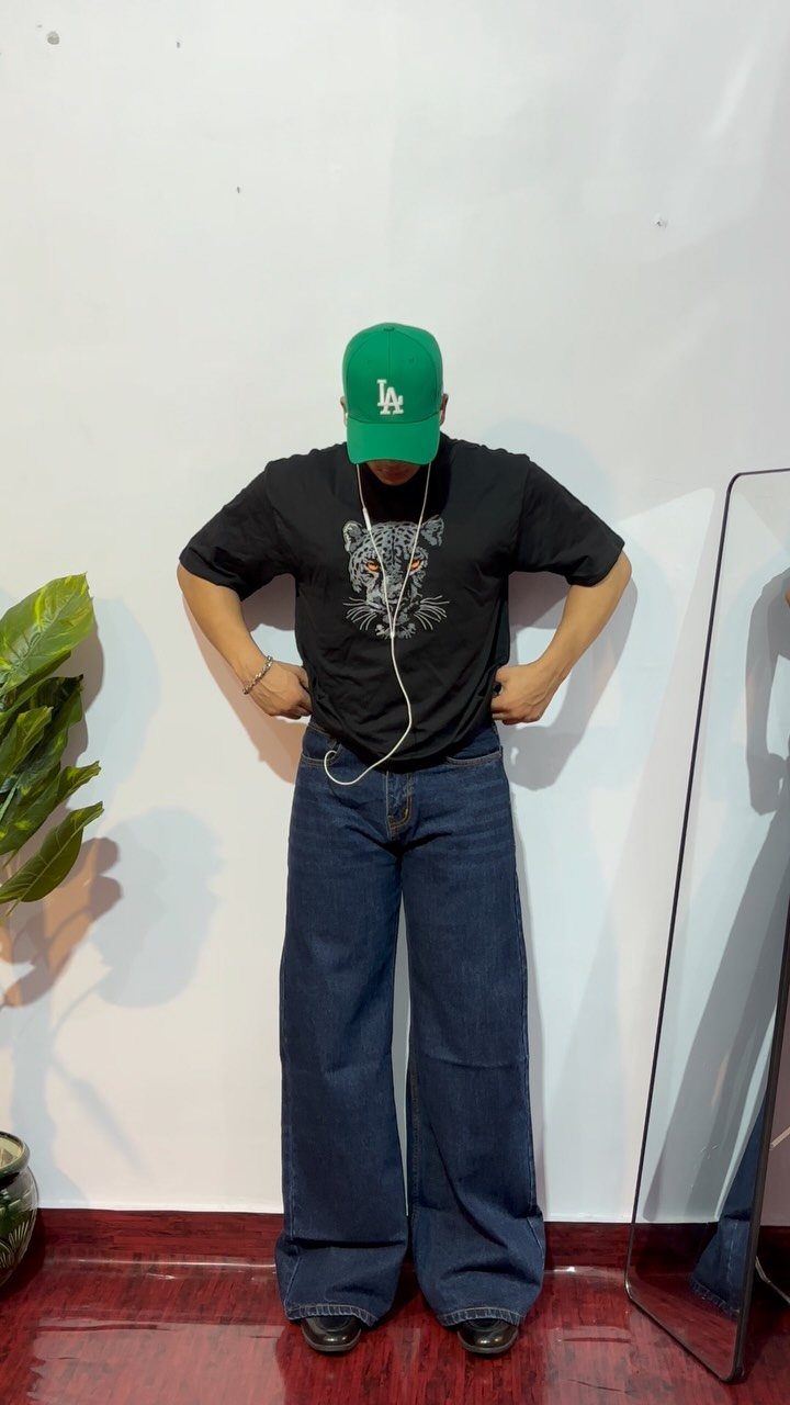 Man wearing a black oversized graphic t-shirt and dark blue baggy denim jeans.
