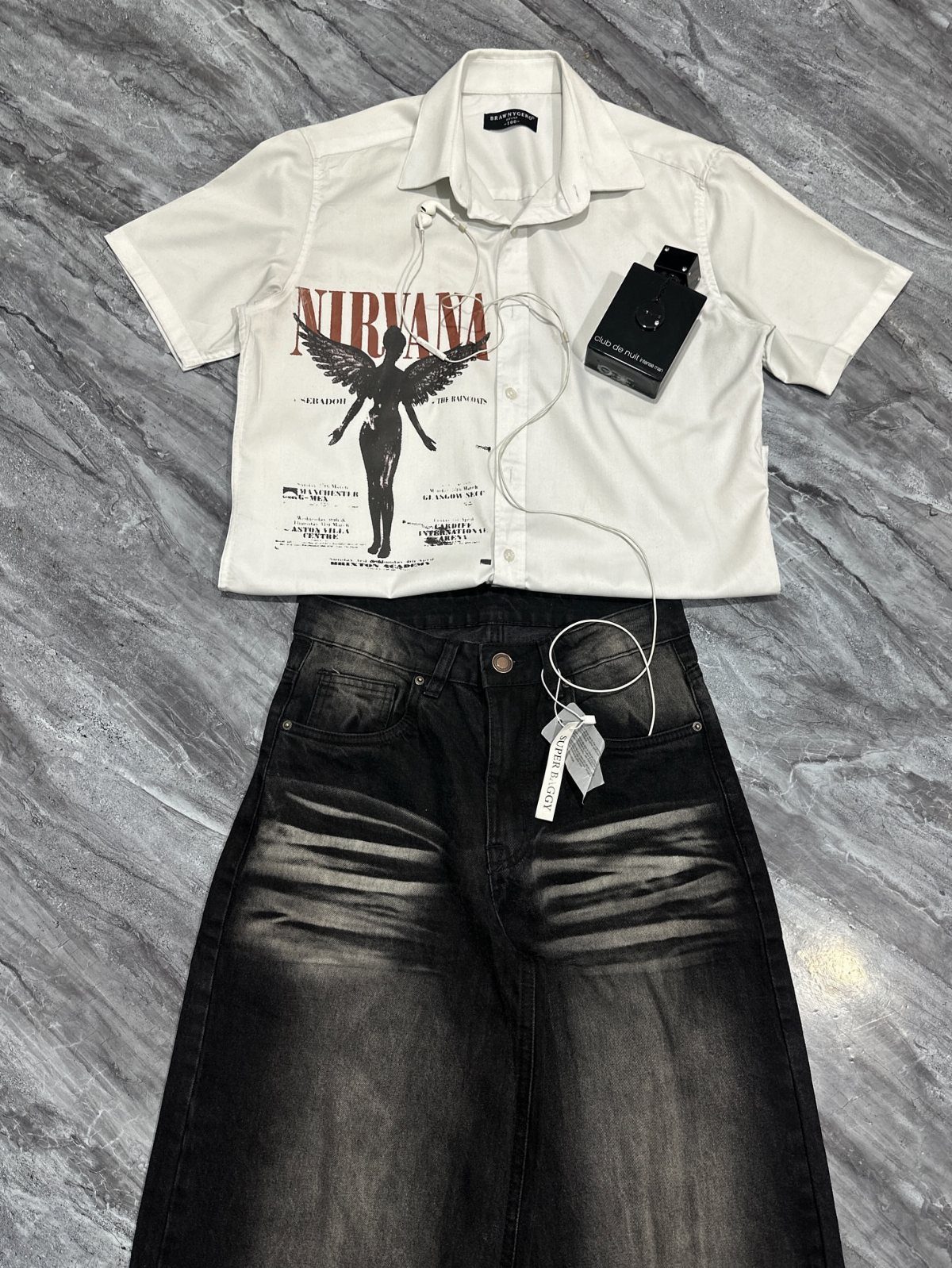 White Nirvana graphic short-sleeve shirt and black faded baggy denim jeans laid on marble.